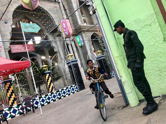 A boy rides a bicycle while looking at an army soldier stationed in front of a Sufi mosque in Kattankudy, Sri Lanka, June 11, 2019. REUTERS/Alexandra Ulmer