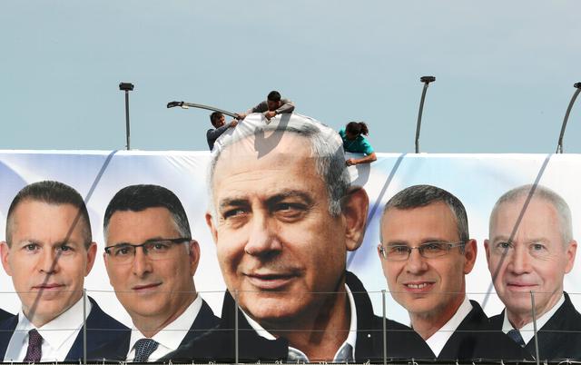 FILE PHOTO: Labourers work on hanging up a Likud election campaign banner depicting Israeli Prime Minister Benjamin Netanyahu with his party candidates, in Jerusalem March 28, 2019. REUTERS/Ammar Awad/File Photo