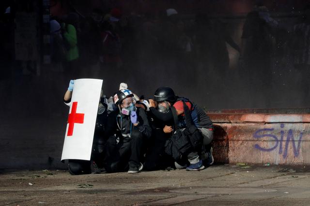 Members of a first aid team and a photographer take cover during an anti-government protest in Santiago, Chile October 28, 2019. REUTERS/Henry Romero     