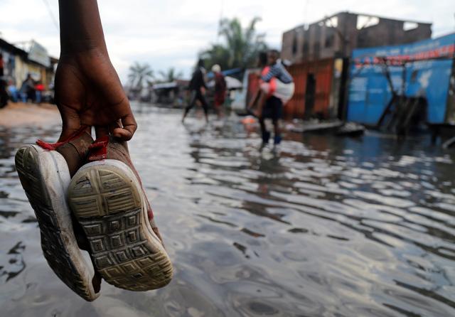 A Congolese man carries his shoes as he wades through floodwaters along a street after the Congo River burst its banks due to heavy rainfall in Kinshasa, Democratic Republic of Congo January 9, 2020. REUTERS/Kenny Katombe