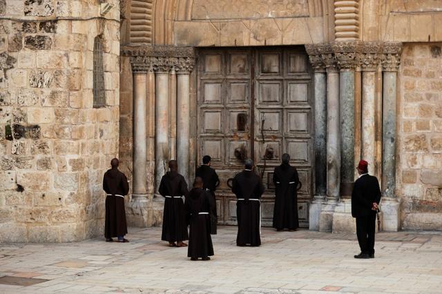 Roman Catholic monks pray in front of the locked door of Jerusalem's Church of the Holy Sepulchre amid coronavirus restrictions in the walled Old City March 27, 2020 REUTERS/ Ammar Awad
